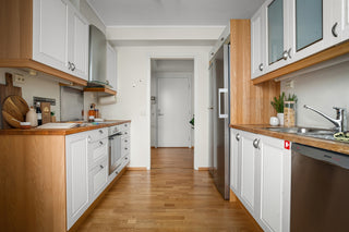 A narrow kitchen with white cabinets and wood floors